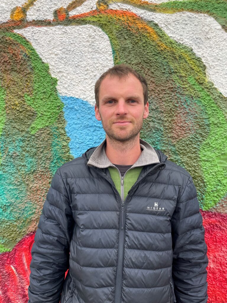 Douglas Ross wearing a black puffer coat standing in front of a wall of street art.